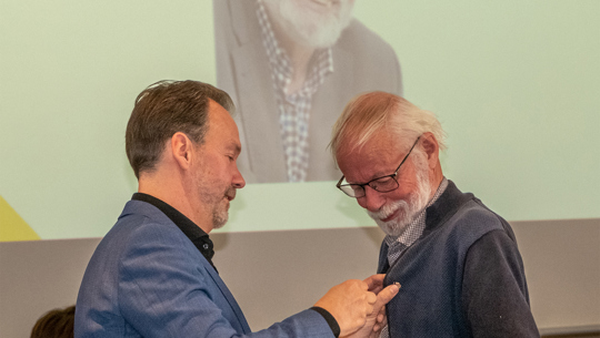 Jaring Roosma kijkt vereerd hoe John Kerstens het lidmaatschap van Verdienste opspeldt.
